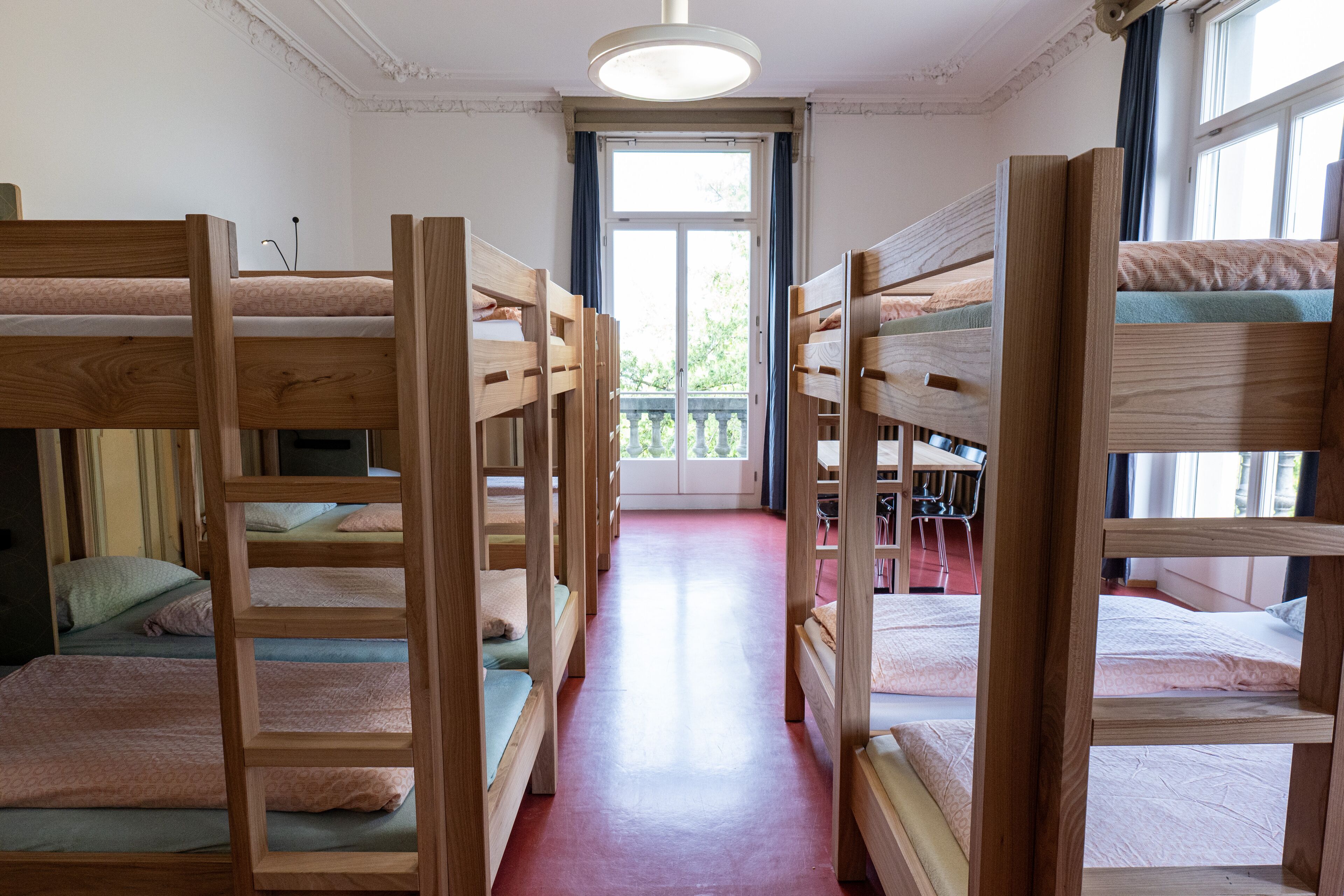 Ein Zimmer mit einer Reihe von Etagenbetten, einem roten Teppich und einem Fenster mit Blick auf Grünfläche.