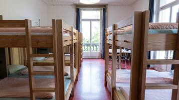 Ein Zimmer mit einer Reihe von Etagenbetten, einem roten Teppich und einem Fenster mit Blick auf Grünfläche.
