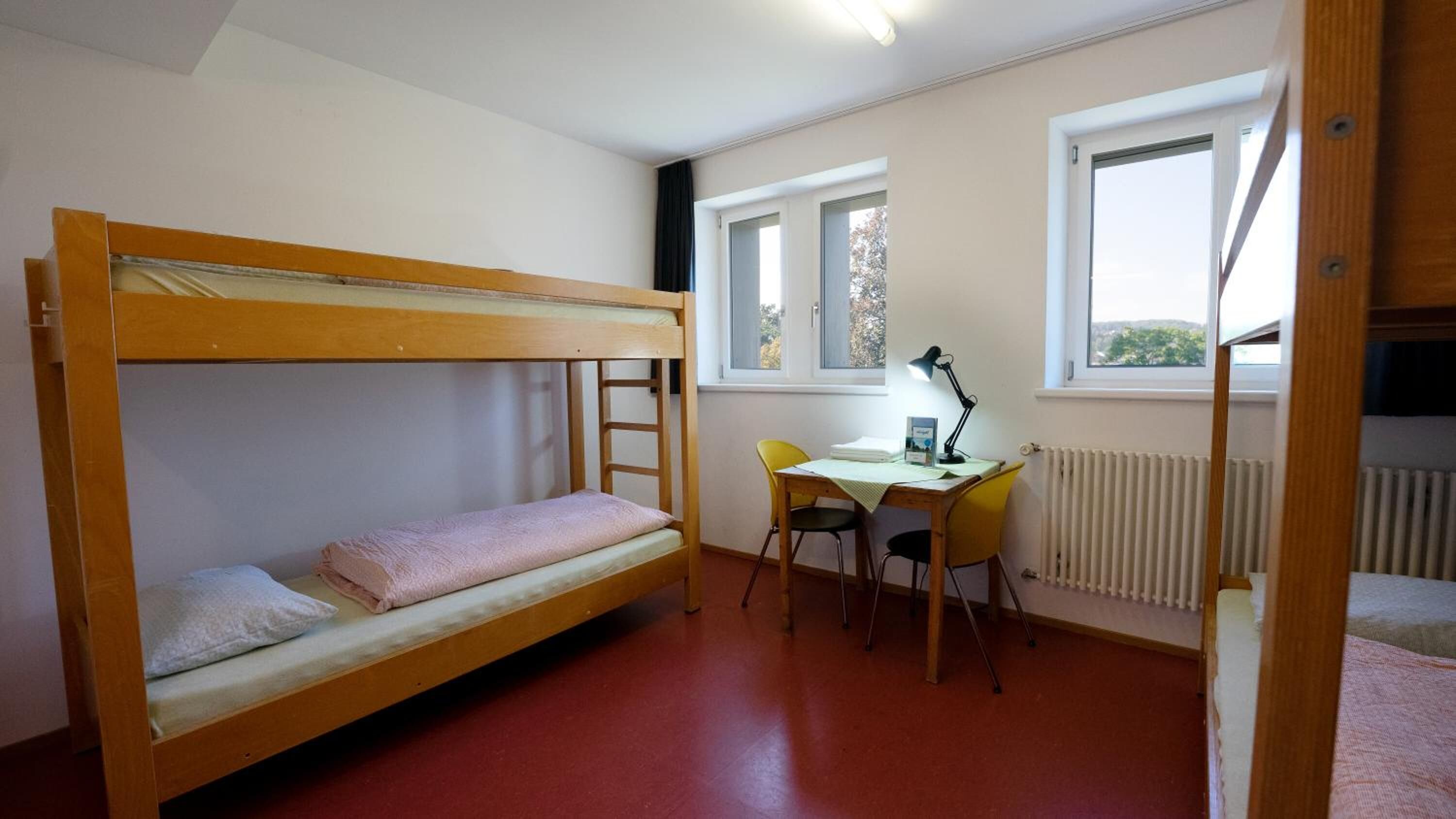 A bunk bed room with a desk and chair, a radiator, and a window.