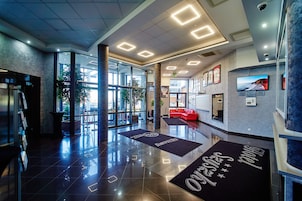 Um lobby de hotel moderno com uma recepção, um sofá vermelho e uma grande janela com vista para o exterior.