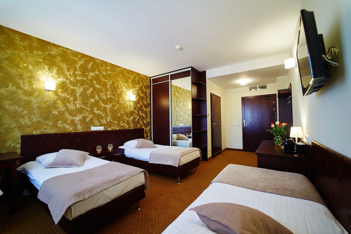 Ein Hotelzimmer mit zwei Betten, einem Kleiderschrank, einem Schreibtisch und einem an der Wand befestigten Fernseher.