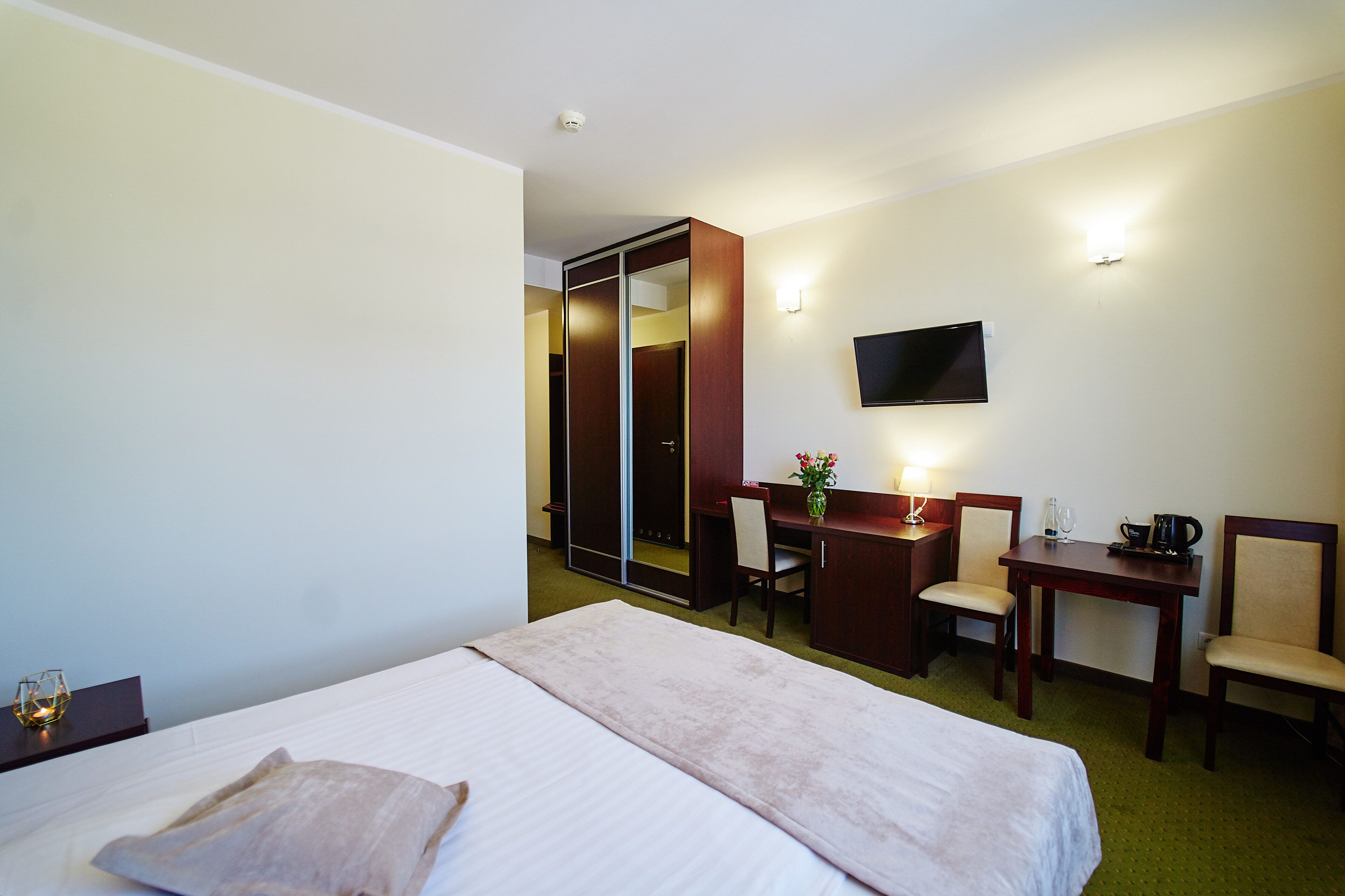 A hotel room with a bed, a desk, a chair, a television, and a mirror.