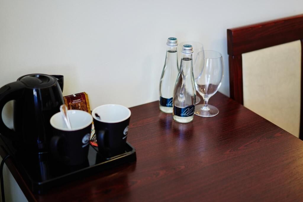 A breakfast tray with a coffee maker, two cups, two bottles of water, and a glass on a wooden table.