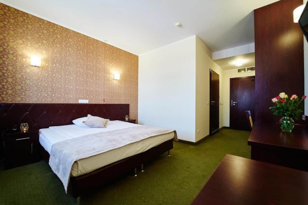Ein Hotelzimmer mit einem großen Bett, einem Nachttisch, einem Schreibtisch und einer wandmontierten Lampe.