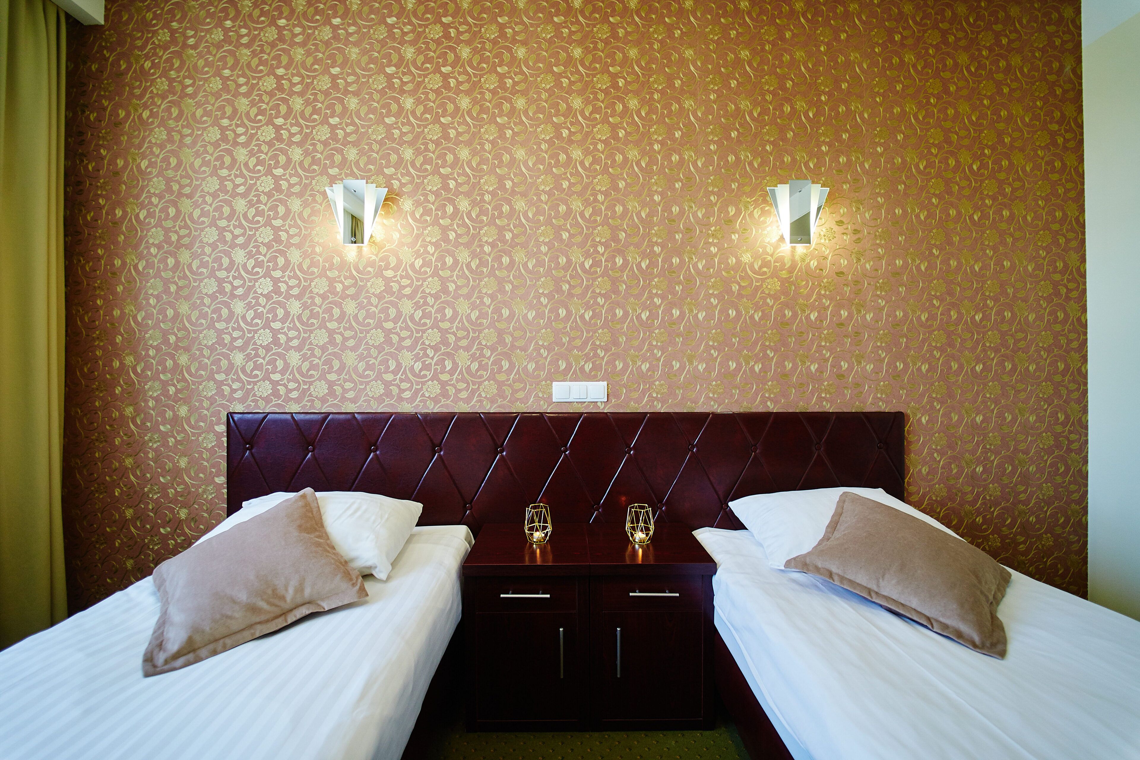 Quarto de hotel com duas camas, um espaldar escuro e arandelas decorativas.