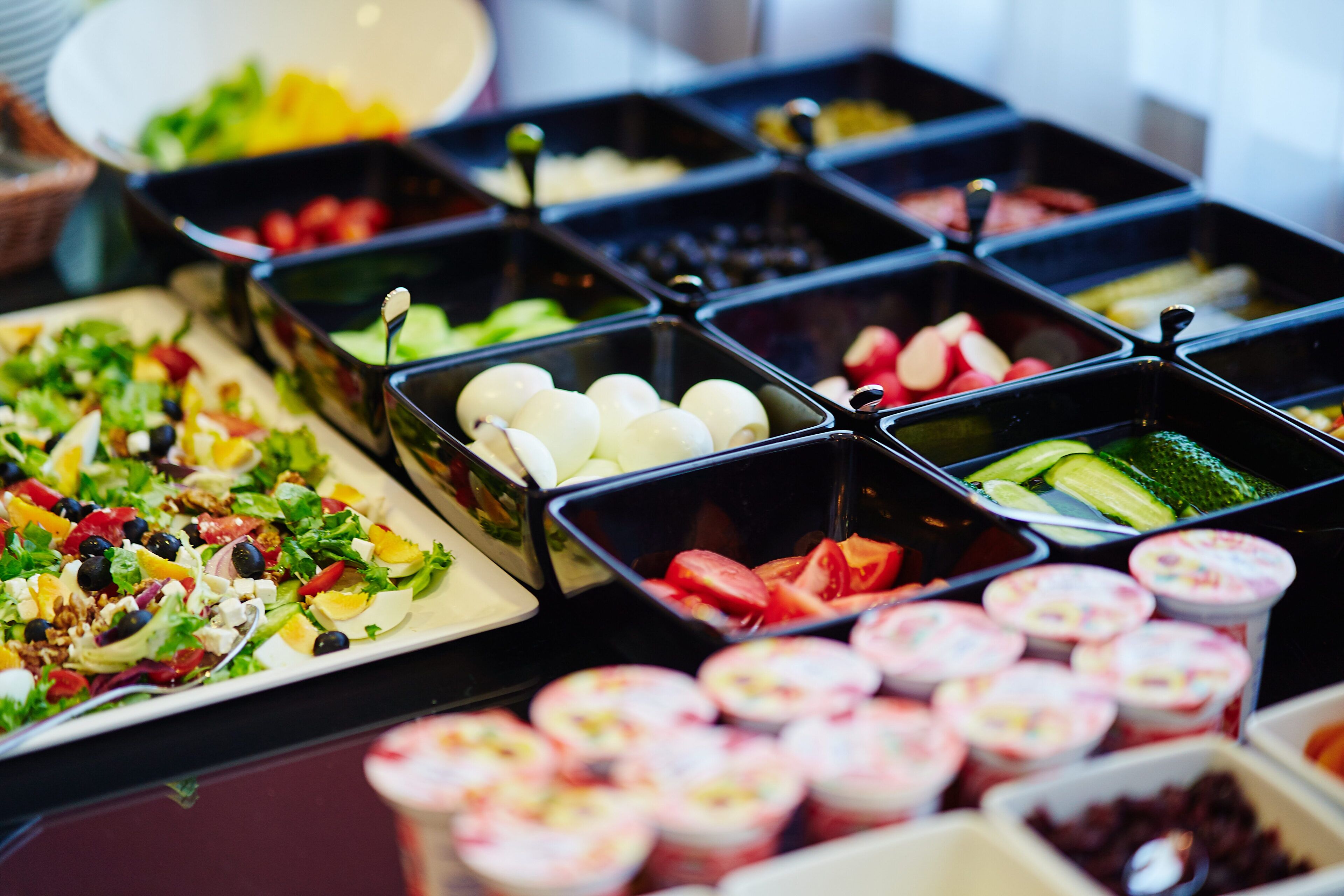 A buffet with various food options including salads, fruits, and yogurt cups.