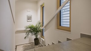 Una escalera con una planta en maceta, un cuadro enmarco y una ventana con persianas.