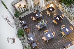 Un patio al aire libre con varias mesas y sillas, rodeado por un muro de piedra y una pared blanca con detalles decorativos.