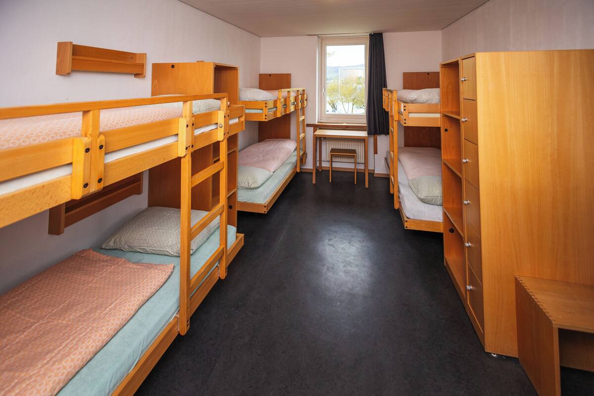 A dormitory room with bunk beds, a desk, and a window.