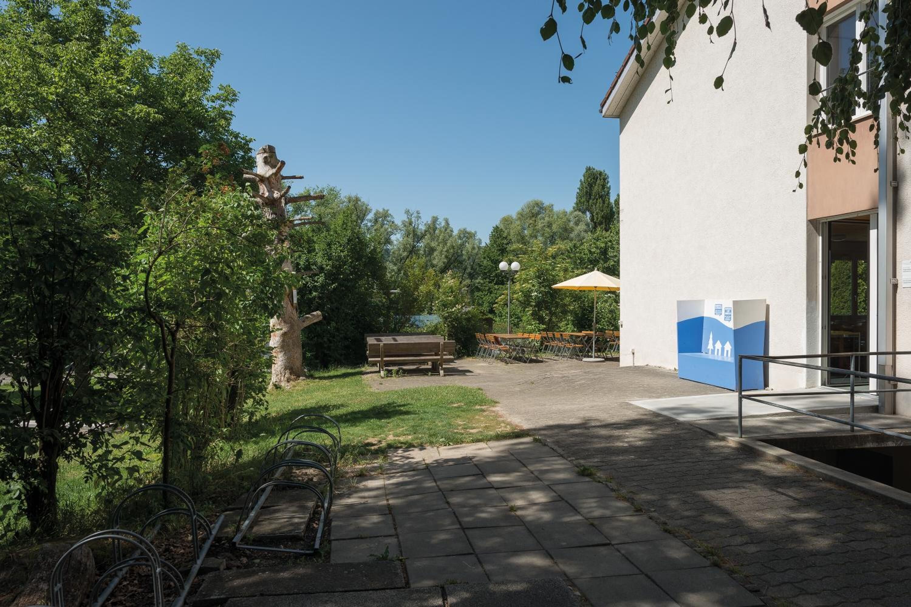 Ein Innenhof mit einer Steinsitzbank, einem Fahrradständer aus Metall und einem Gebäude mit einer blau-weißen Beschilderung.