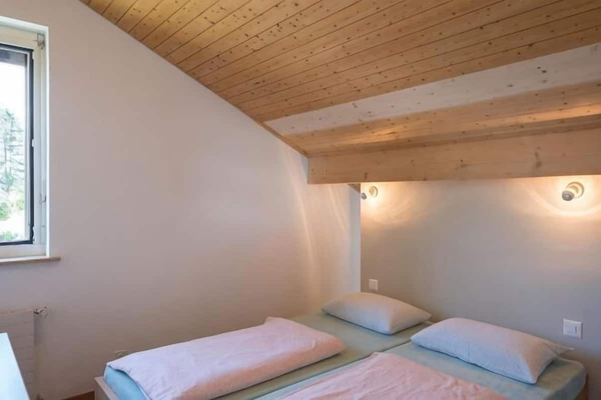 A room with two beds, wooden ceiling beams, and a window.