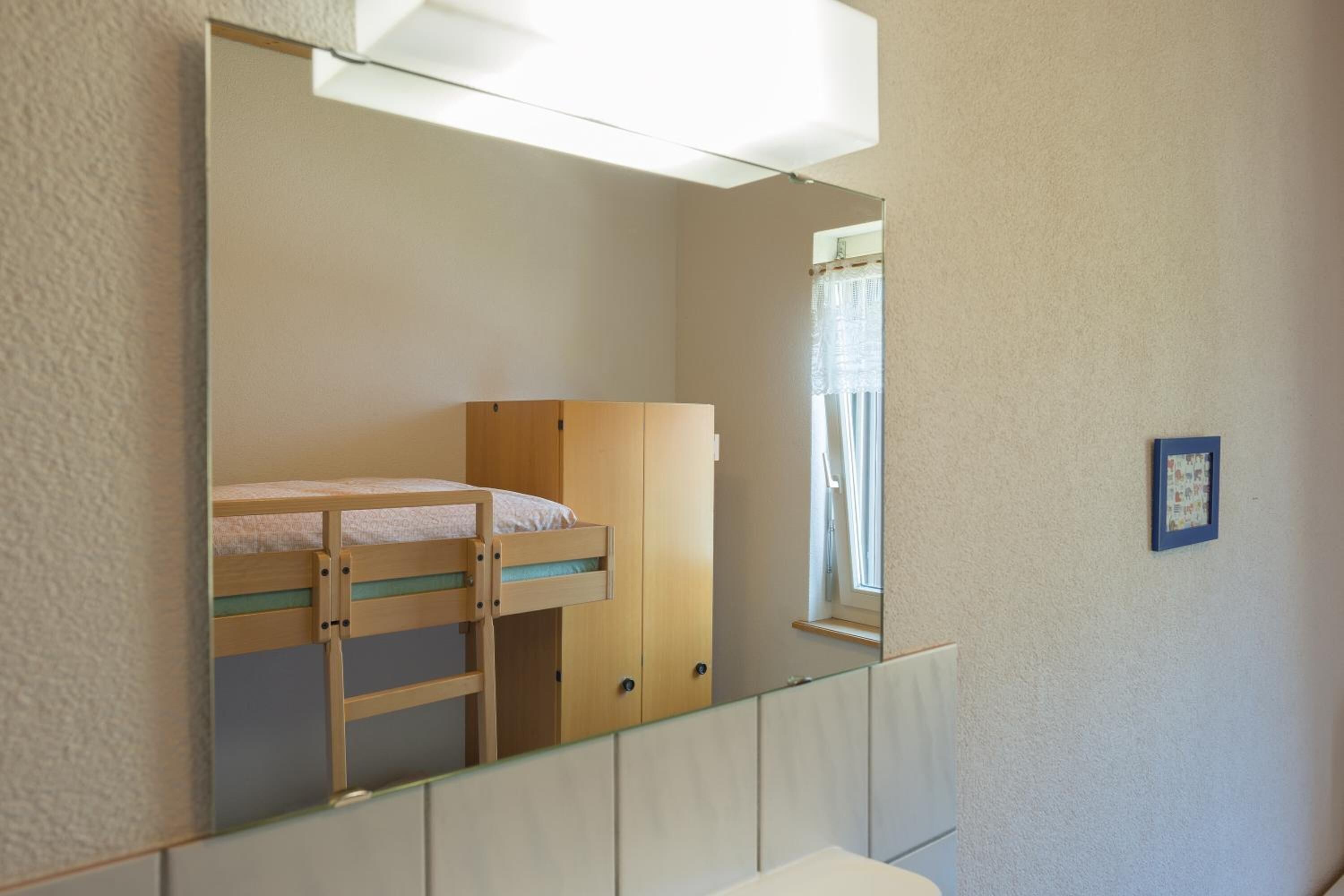 Une chambre avec un lit superposé, une armoire et un miroir.