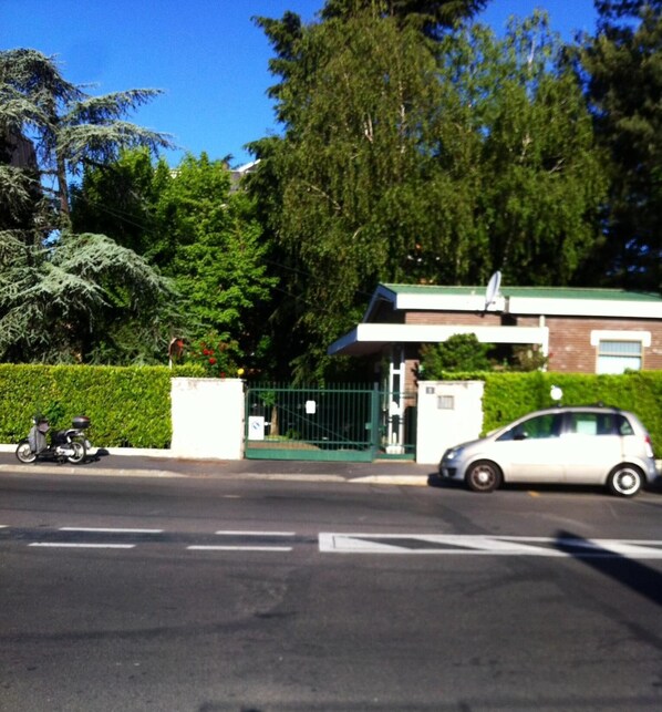Una entrada con portón, un portón verde, un coche estacionado y una motocicleta al borde de la carretera.