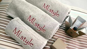 Three folded towels with "M.style" embroidered on them, placed on a striped bedspread. - MI.style (Milan)