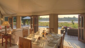 A tented accommodation with a dining area, sofas, and a view of the outdoors.