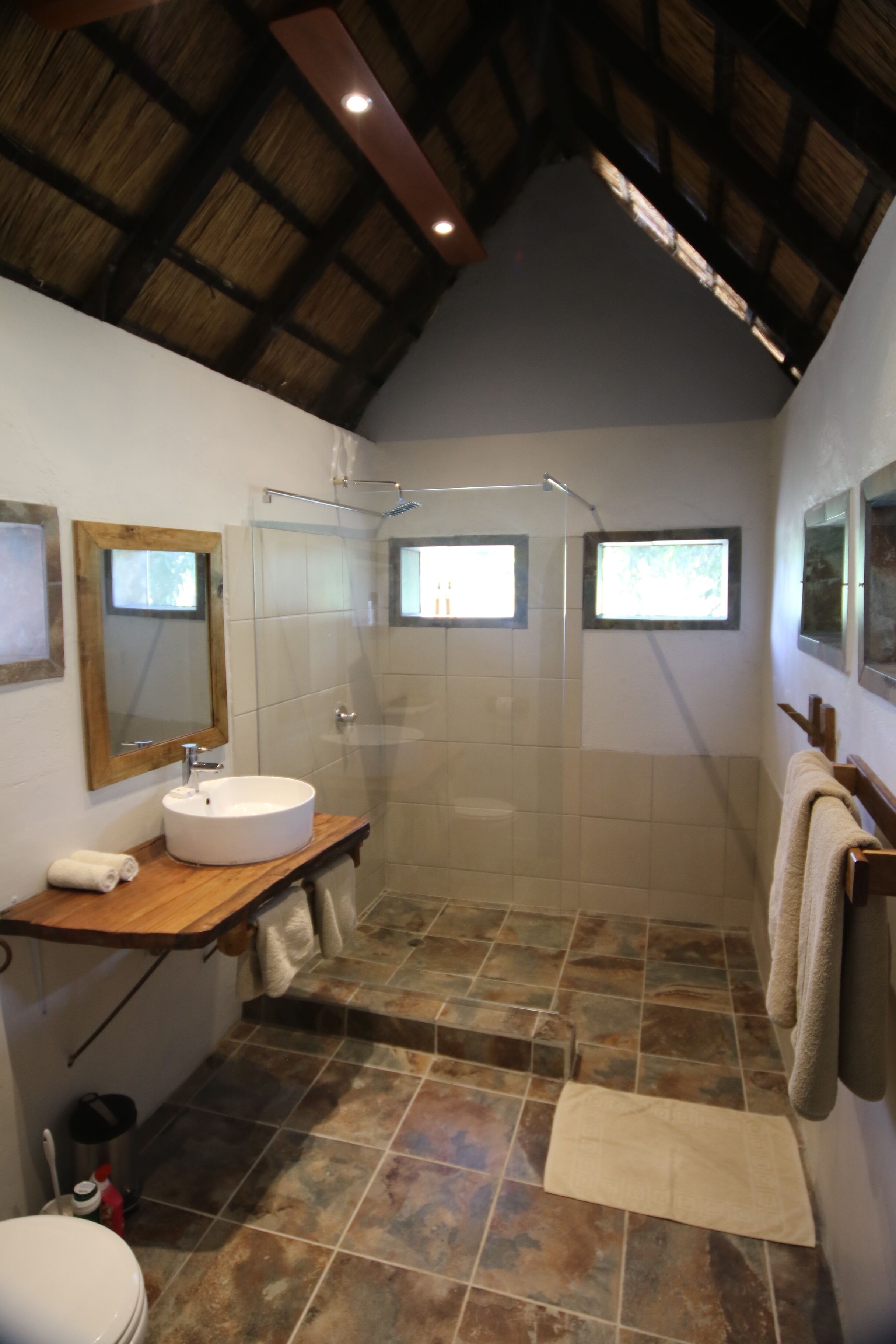 Un bagno con un mobile bagno in legno, un lavandino bianco, una cabina doccia in vetro e un pavimento piastrellato.