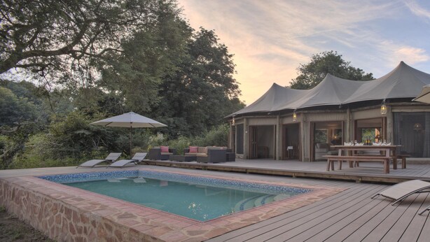 A poolside area with lounge chairs, a hot tub, and a covered seating area with umbrellas.