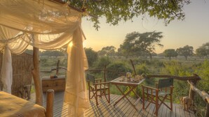 A rustic wooden deck with a table set for two, surrounded by wooden chairs, overlooking a grassy landscape with trees.