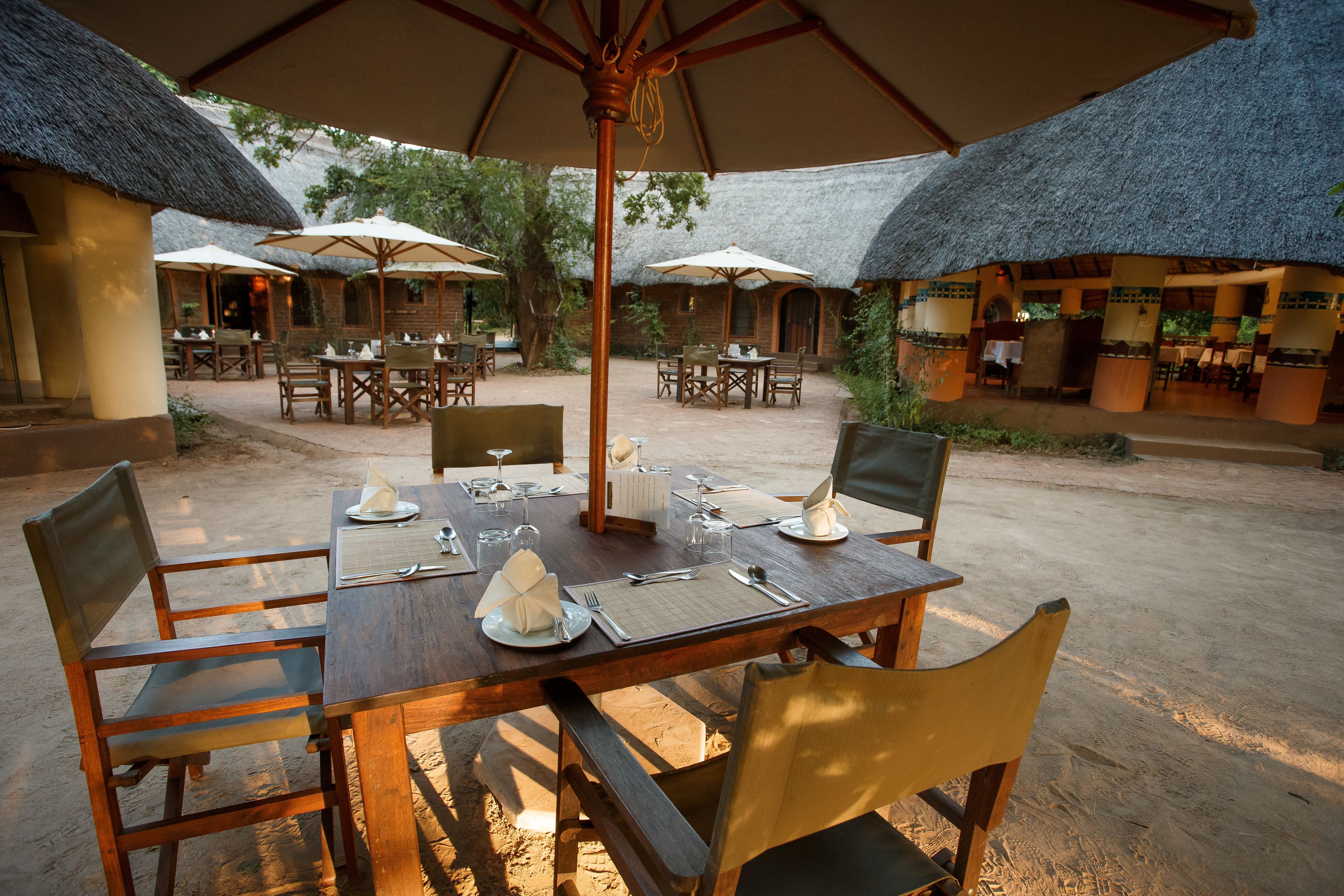 Een buitenterras met houten tafels en stoelen, rieten constructies en parasols voor beschutting.