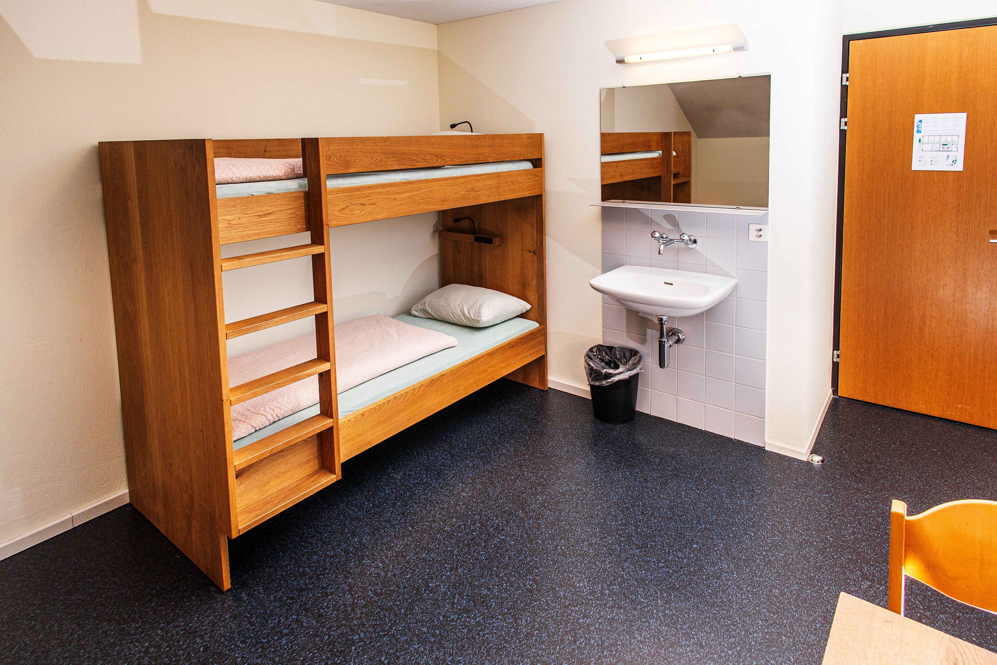 Een stapelbed met houten frame en een kleine badkamer met wastafel en spiegel.