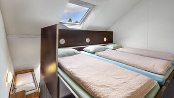 A dormitory-style room with bunk beds, a skylight, and a small wooden desk.