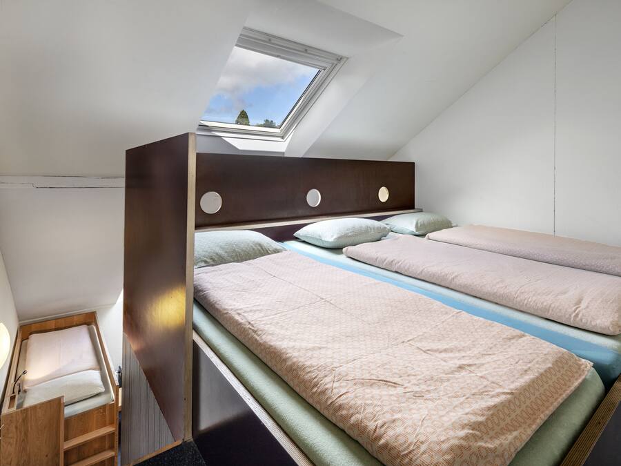 A dormitory-style room with bunk beds, a skylight, and a small wooden desk.