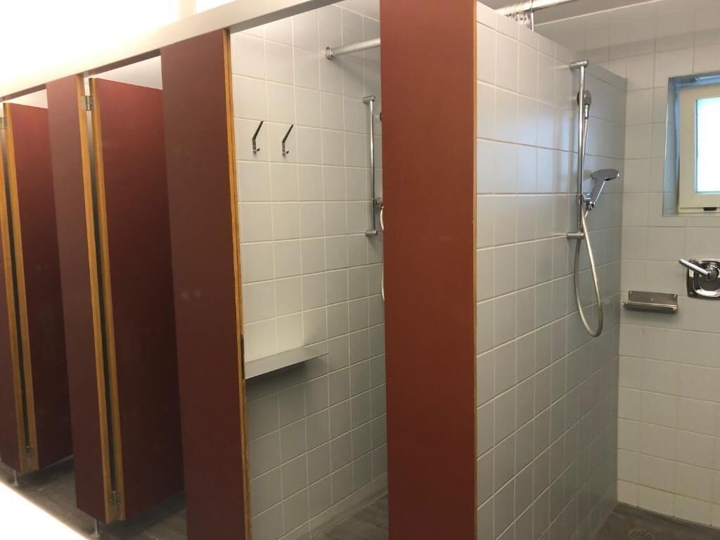 A row of red and white tiled shower stalls with a hand dryer and a towel rack.