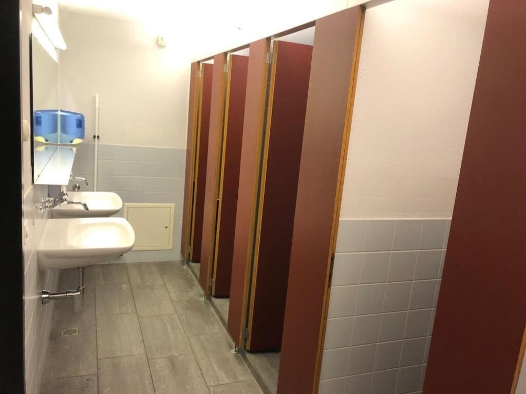 A public restroom with two sinks, a mirror, and a row of stalls.