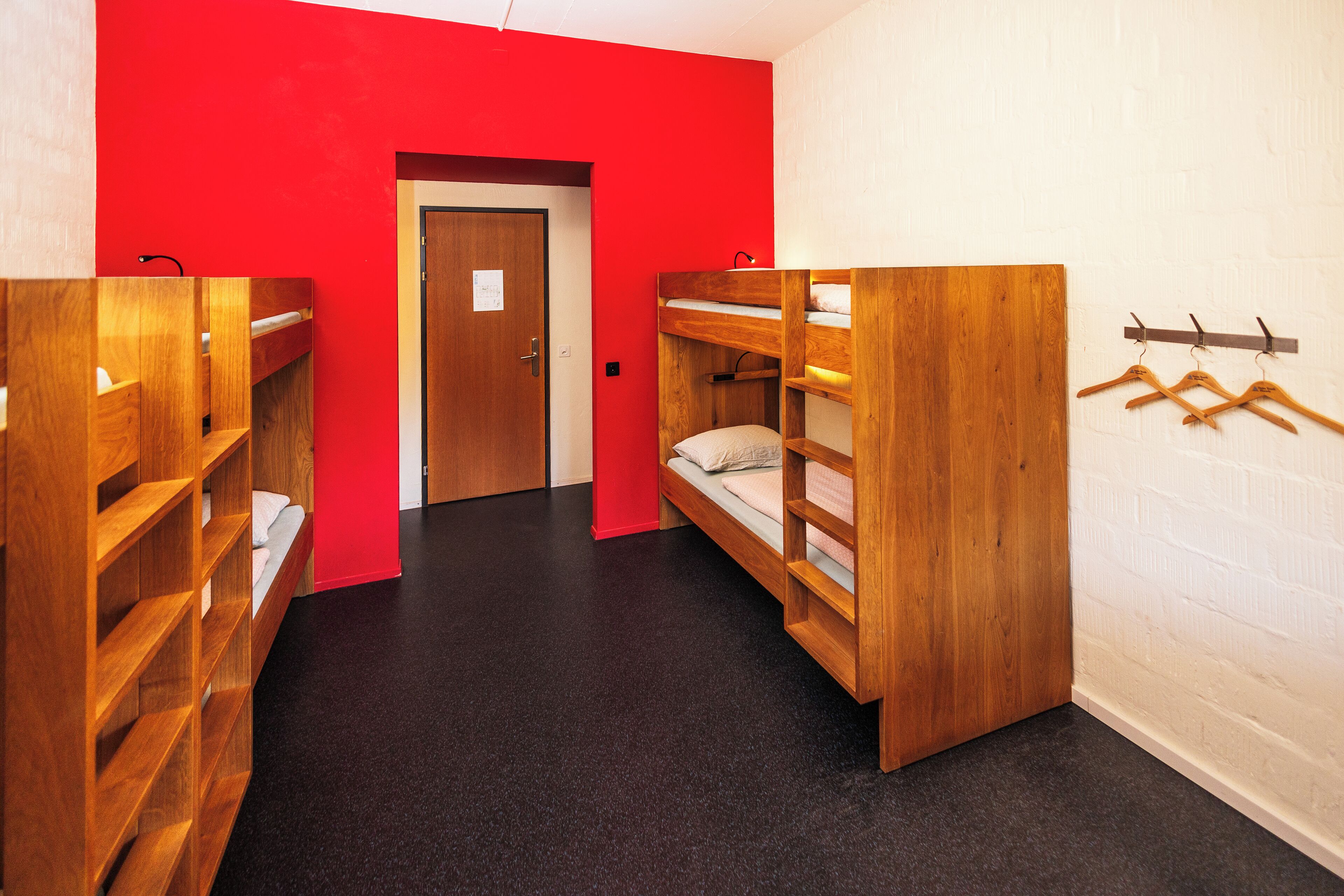 A dormitory room with bunk beds, a wooden wardrobe, and a coat rack.