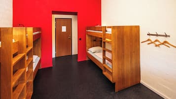 A dormitory room with bunk beds, a wooden wardrobe, and a coat rack.