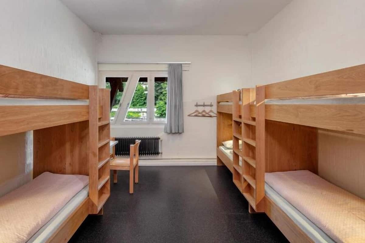 A room with bunk beds, a radiator, a window with curtains, and a chair.