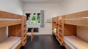 Ein Zimmer mit Etagenbetten, einem Heizkörper, einem Fenster mit Vorhängen und einem Stuhl.