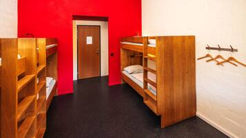 Un dormitorio con literas, una puerta y un perchero con ganchos.