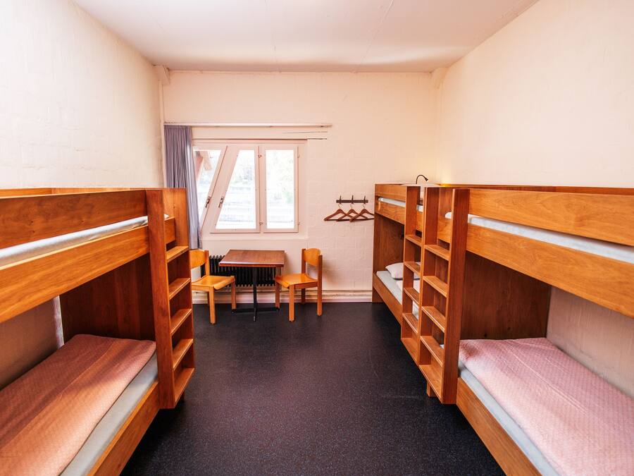Ein Schlafsaalzimmer mit Etagenbetten, einem Tisch, Stühlen und einer Heizung.