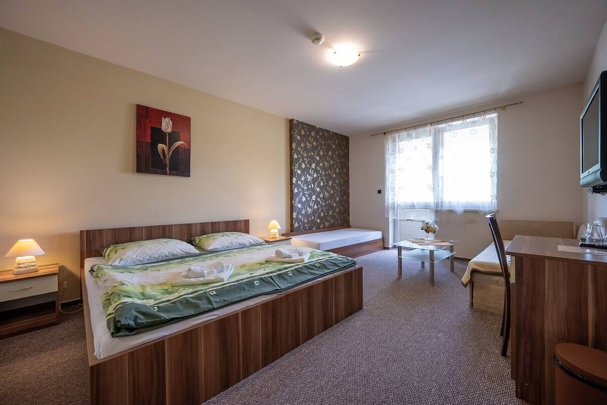 Une chambre d’hôtel comprenant un lit, une table de chevet, une lampe, une fenêtre avec des rideaux et une petite table avec une chaise.