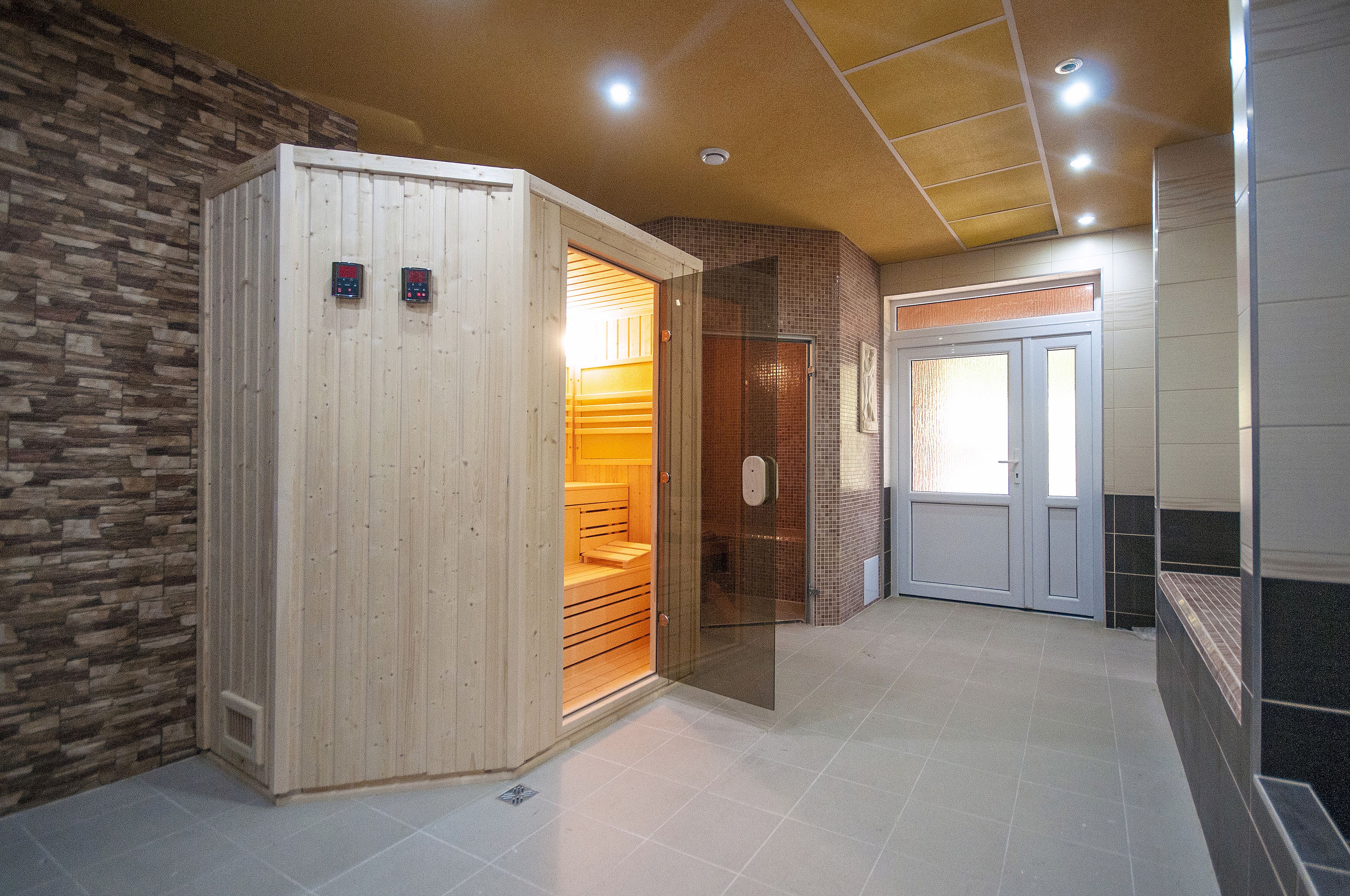 A sauna room with a wooden door, a tiled floor, and a stone wall.