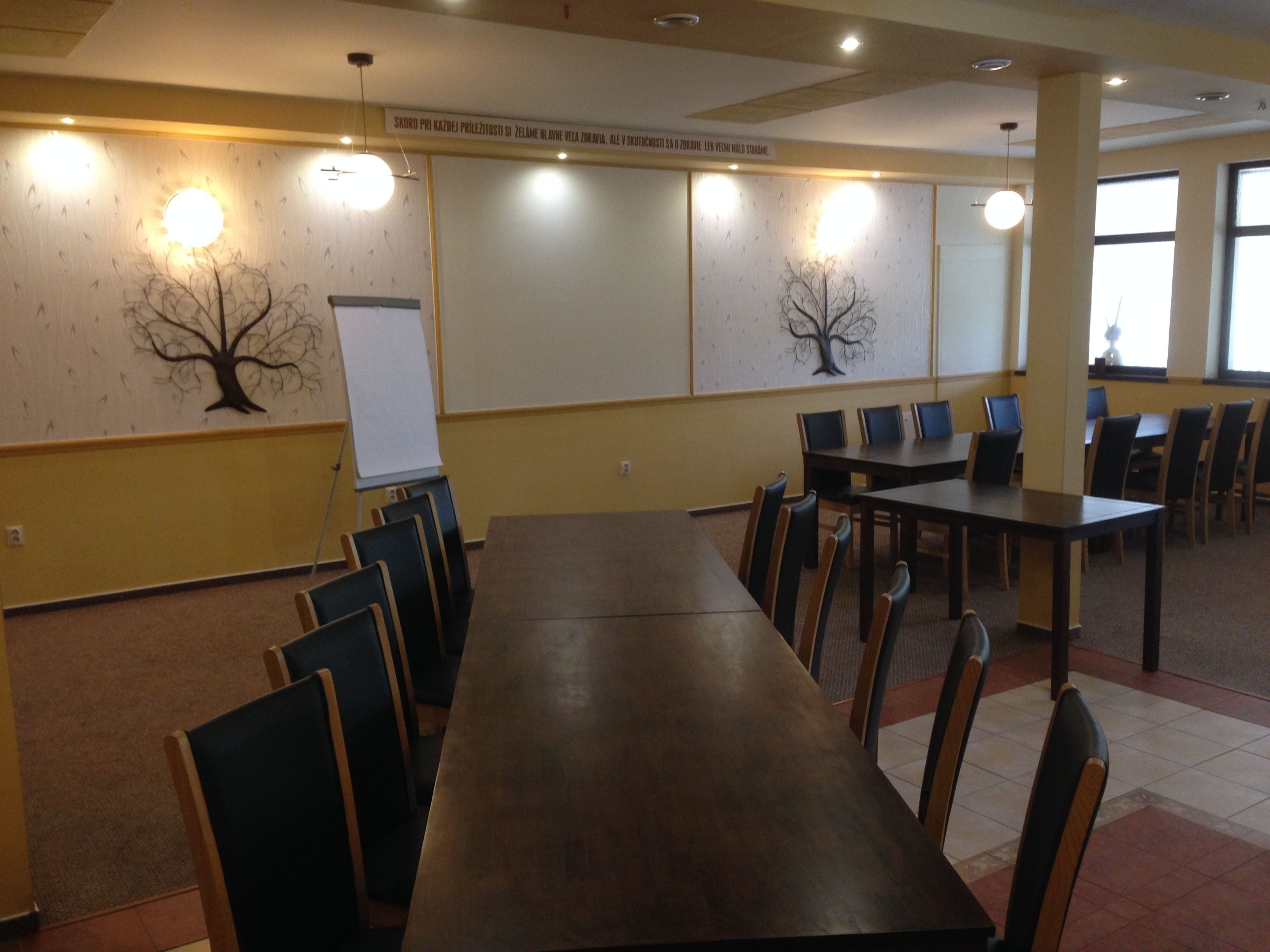 A conference room with a long table and chairs, a whiteboard, and wall-mounted light fixtures.