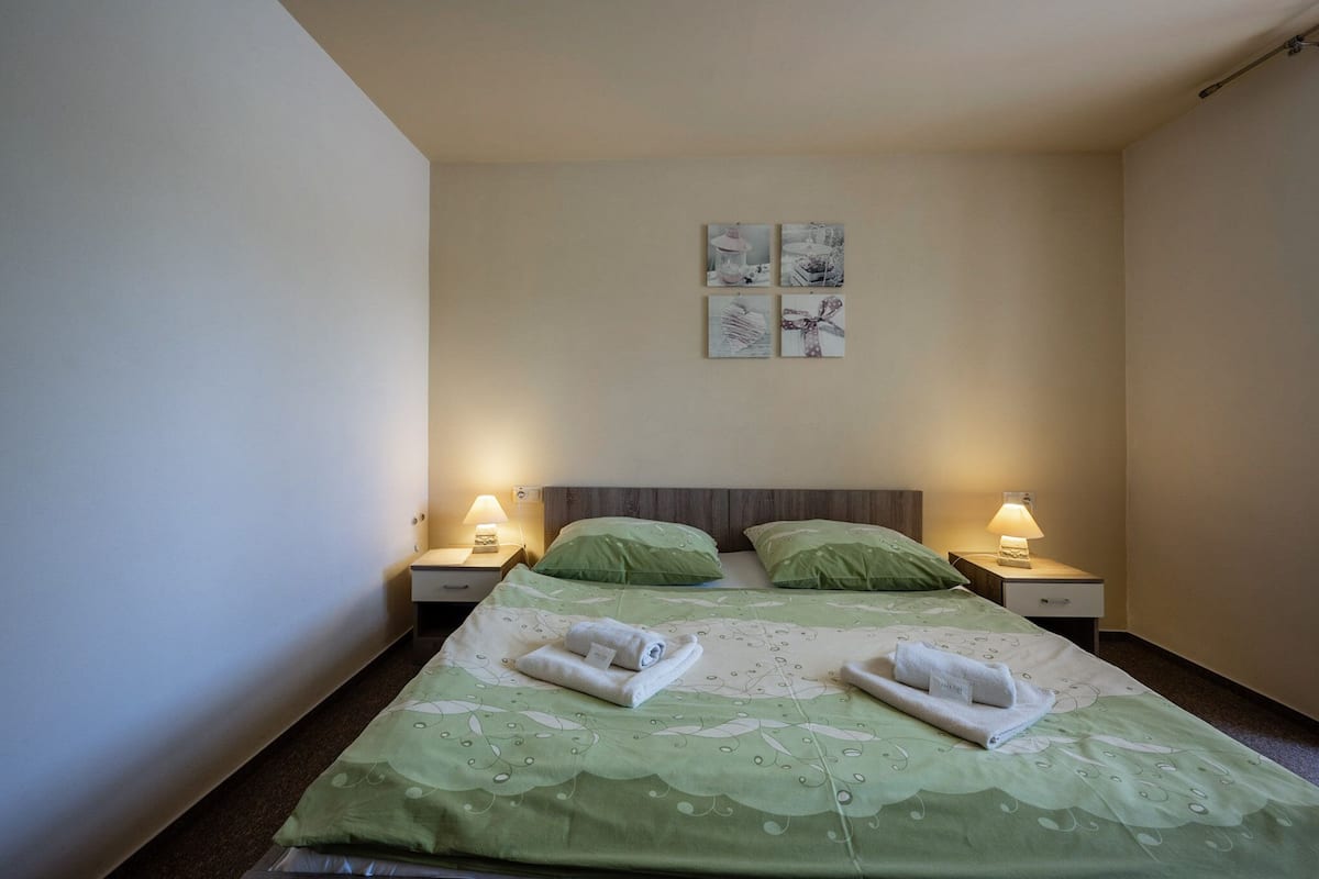 Une chambre d’hôtel avec deux lits, une literie verte, deux tables de chevet avec des lampes et un mur orné de trois tableaux encadrés.
