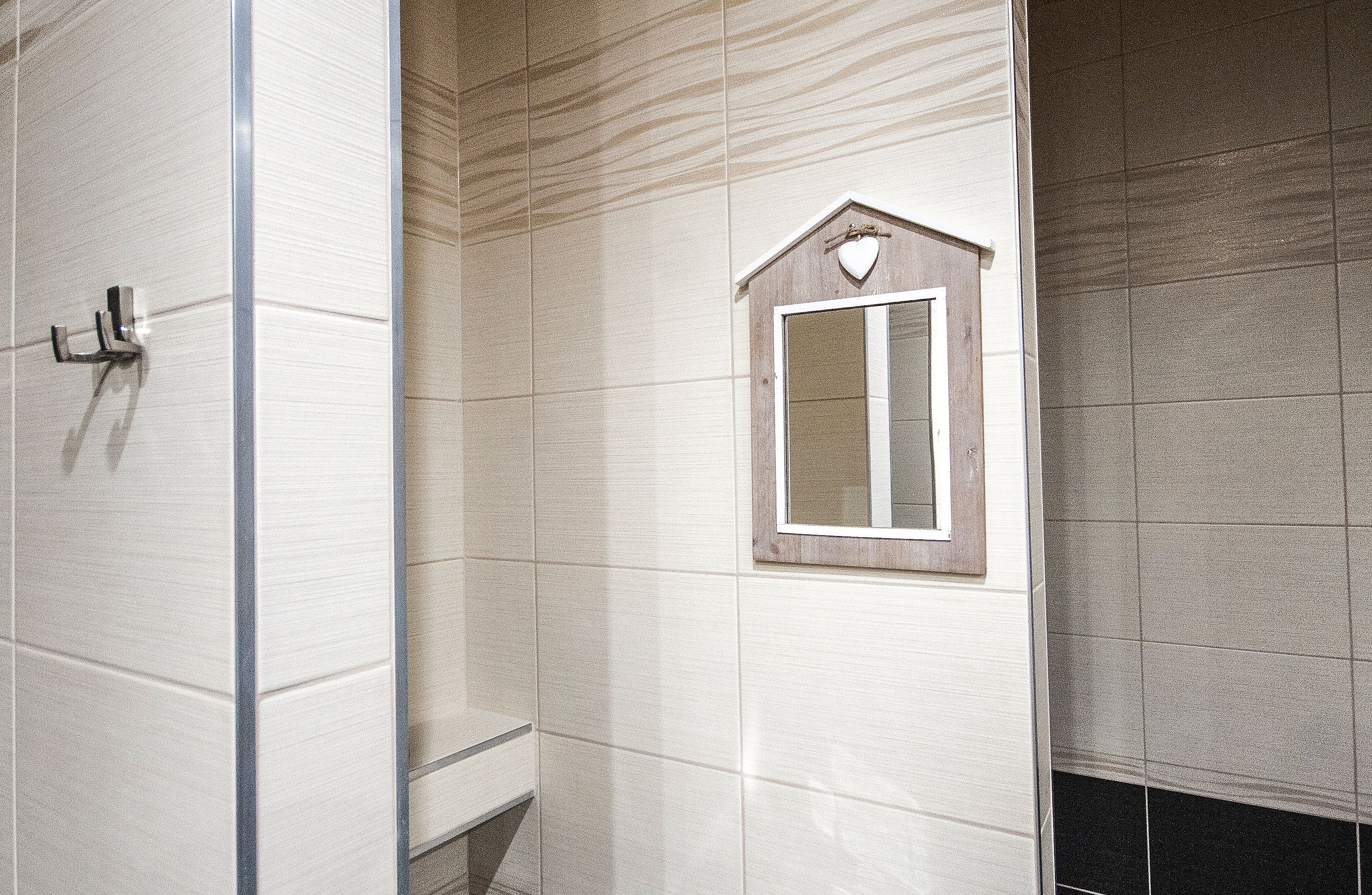 Une salle de bain avec des murs carrelés de carreaux blancs, un miroir à cadre en bois et un espace douche.