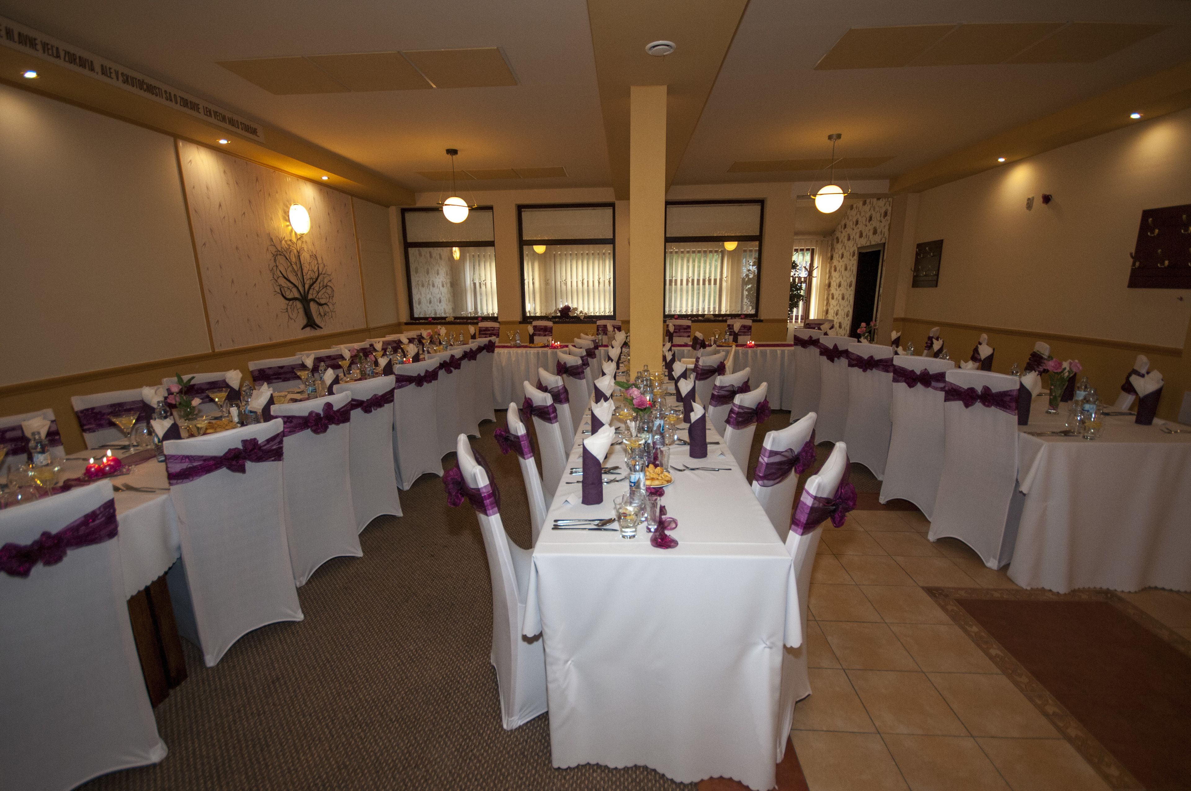 A banquet hall with long tables set for a formal event, featuring white tablecloths and purple sashes.