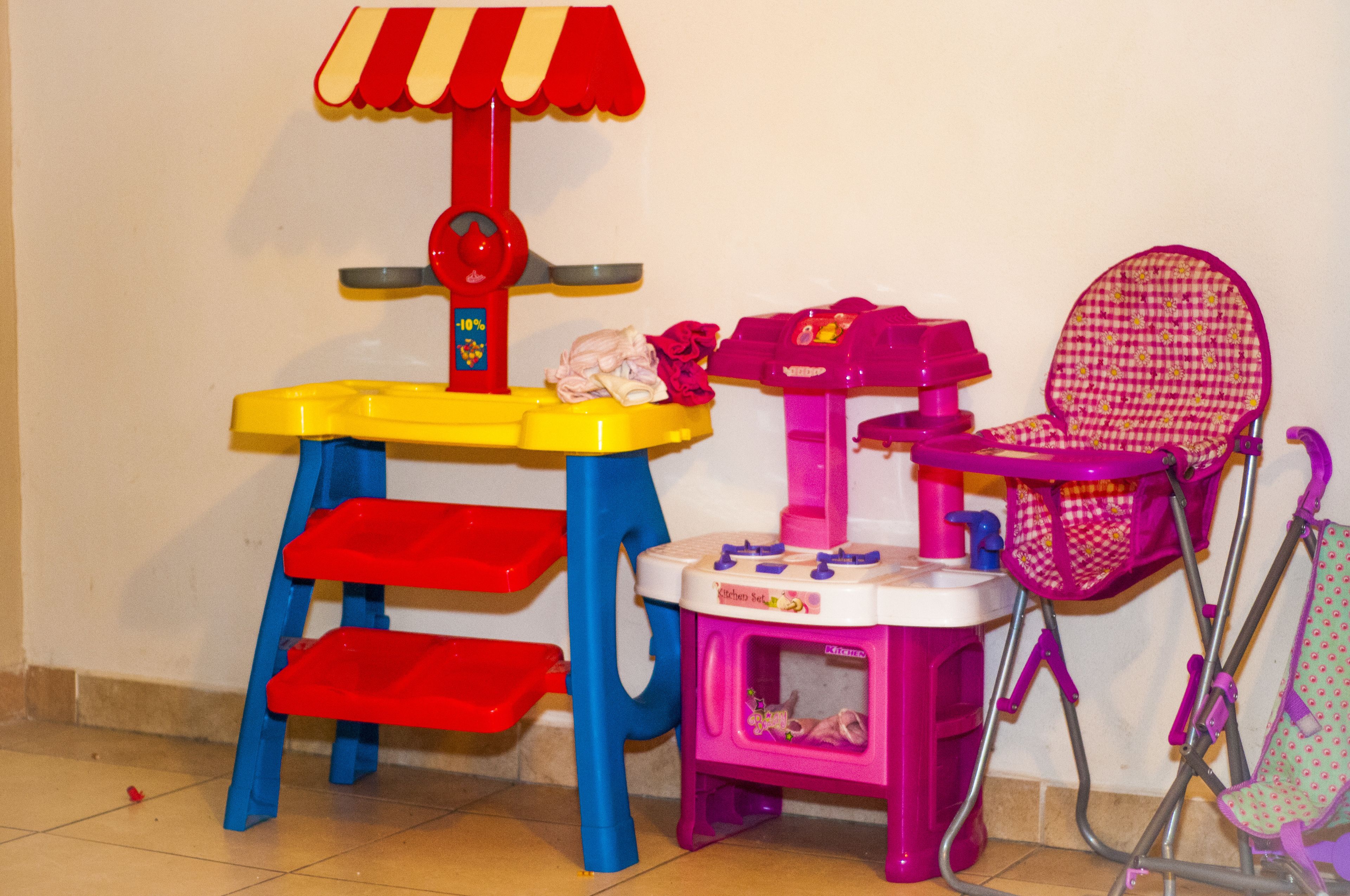 A children's play area with a small table, a toy food stand, and a pink chair.