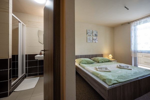 A bedroom with a bed, a nightstand, a wall-mounted light, and a window with blinds. - Penzion Zivka (Zavazna Poruba)