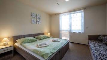Une chambre à coucher avec un lit, deux tables de chevet avec des lampes, une fenêtre avec des rideaux et un canapé.