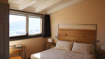 Una camera da letto con testiera in legno, un letto con due cuscini, un comodino, una scrivania con sedia e una finestra vista città.