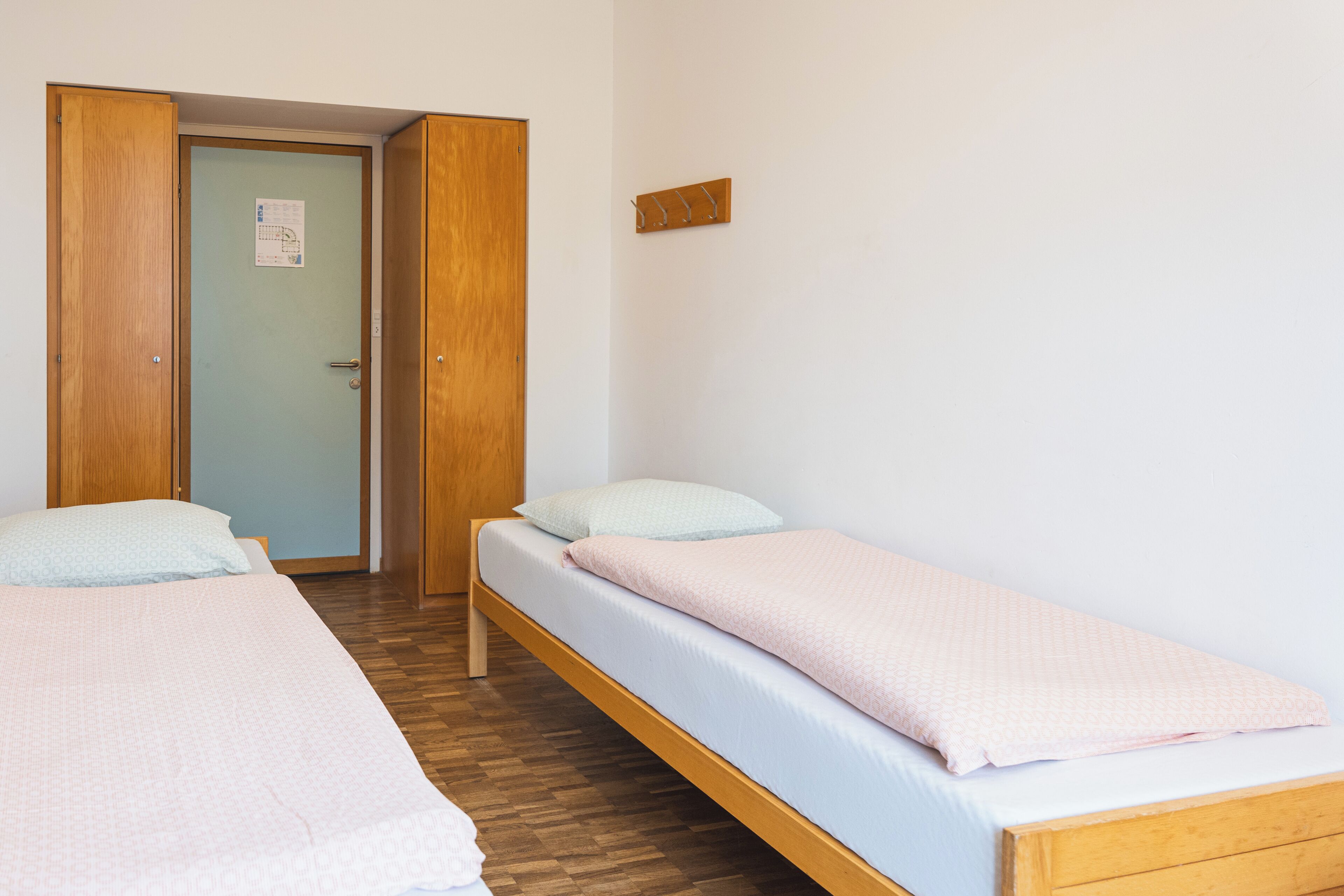 Una habitación con dos camas individuales, piso de madera y una puerta con un letrero.