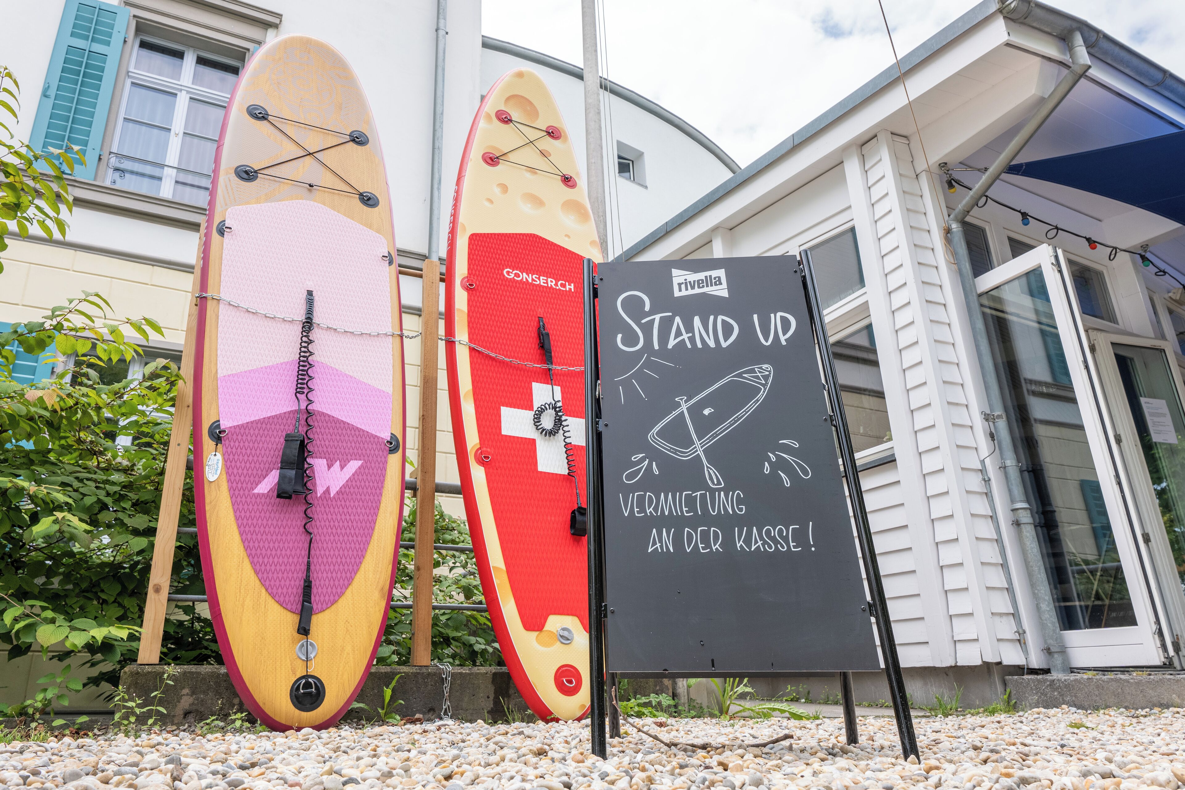 Two surfboards leaning against a building with a sign that reads "Stand Up" and "Verwendung an der Kasse!"