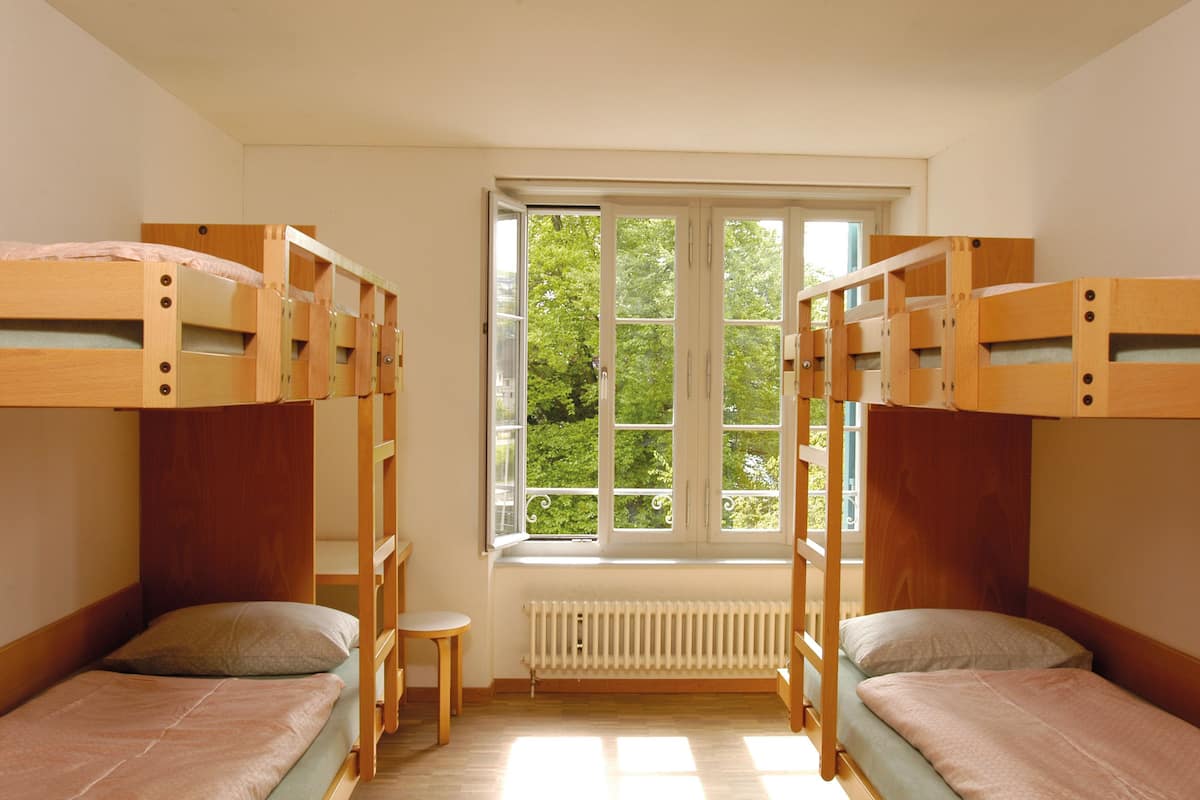 Ein Zimmer mit Etagenbetten, einem kleinen Tisch und einem Fenster mit Blick auf Grünflächen.