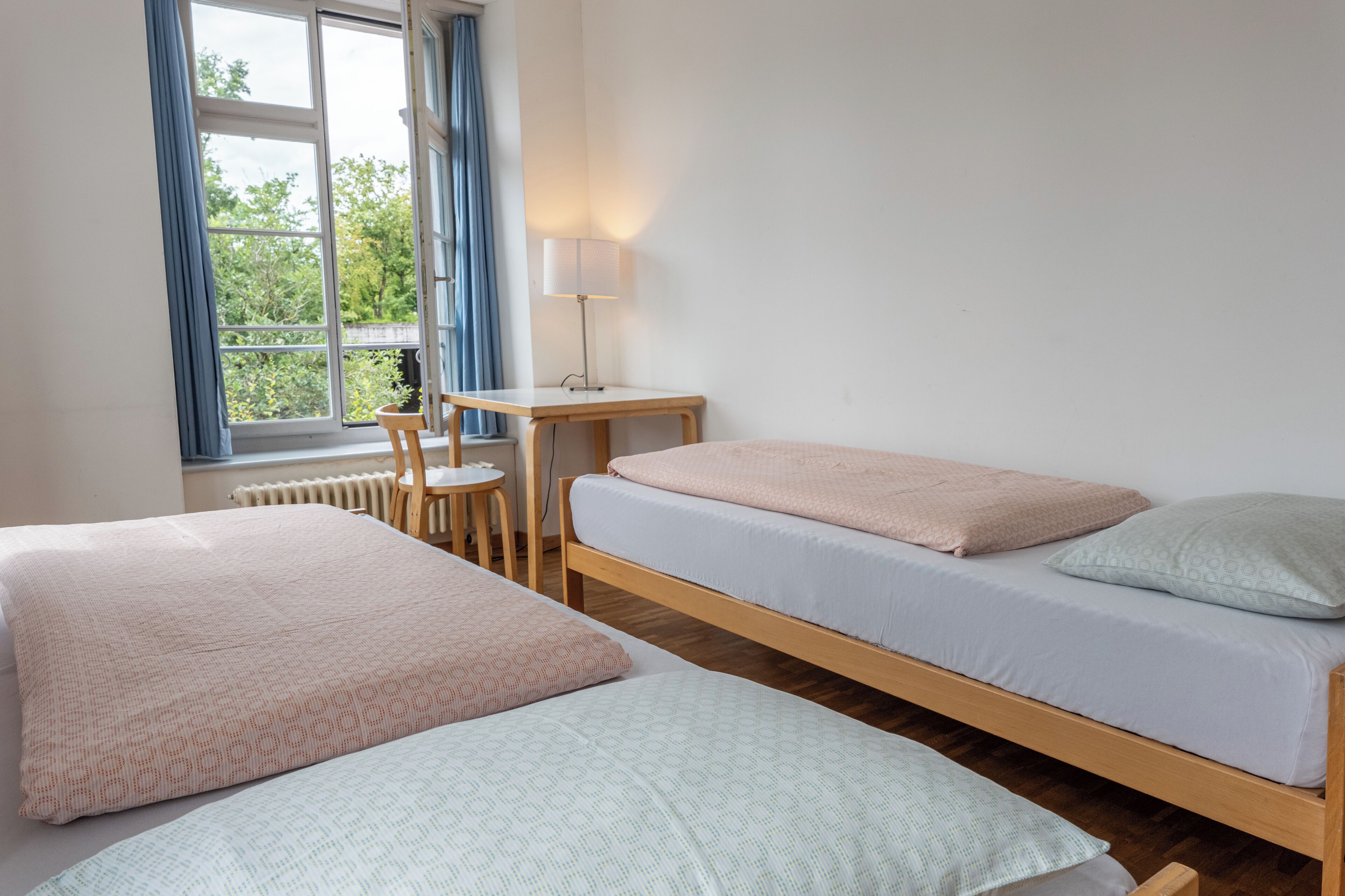 Une chambre avec deux lits simples, une petite table avec une lampe et une fenêtre avec des rideaux.