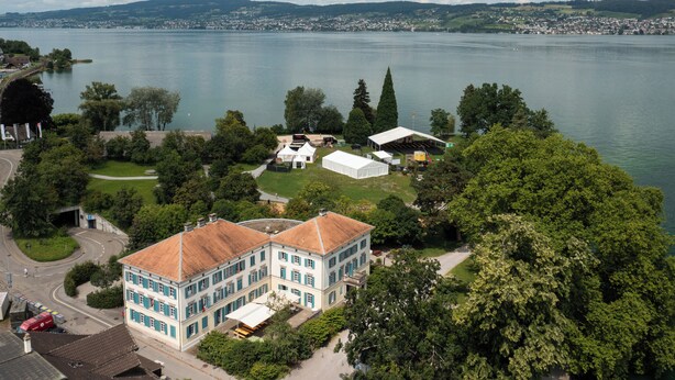 A large building with a red roof, surrounded by trees and a lake. - Youth Hostel Richterswil (Richterswil)