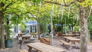 An outdoor seating area with wooden picnic tables and benches, surrounded by trees and covered by a pergola. - Youth Hostel Richterswil (Richterswil)